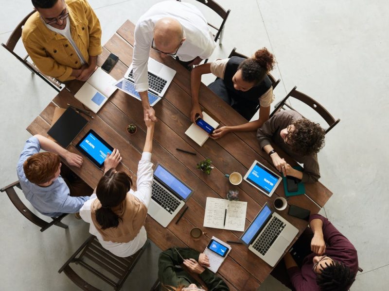 Grupo de ocho personas reunidas trabajando en una mesa con laptops.